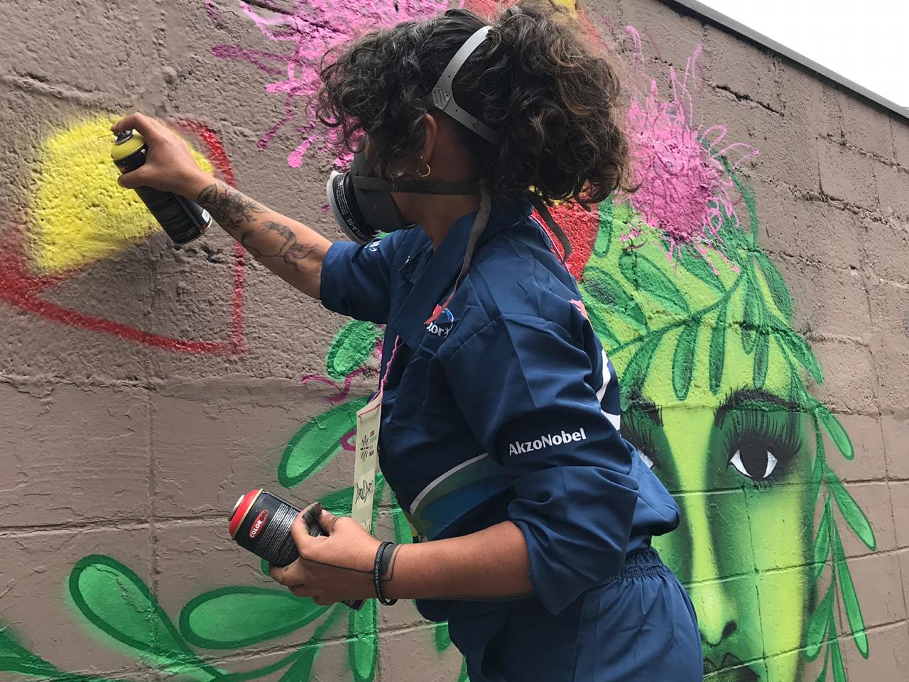Imagem mostra grafiteira fazendo uma pintura no muro da rua